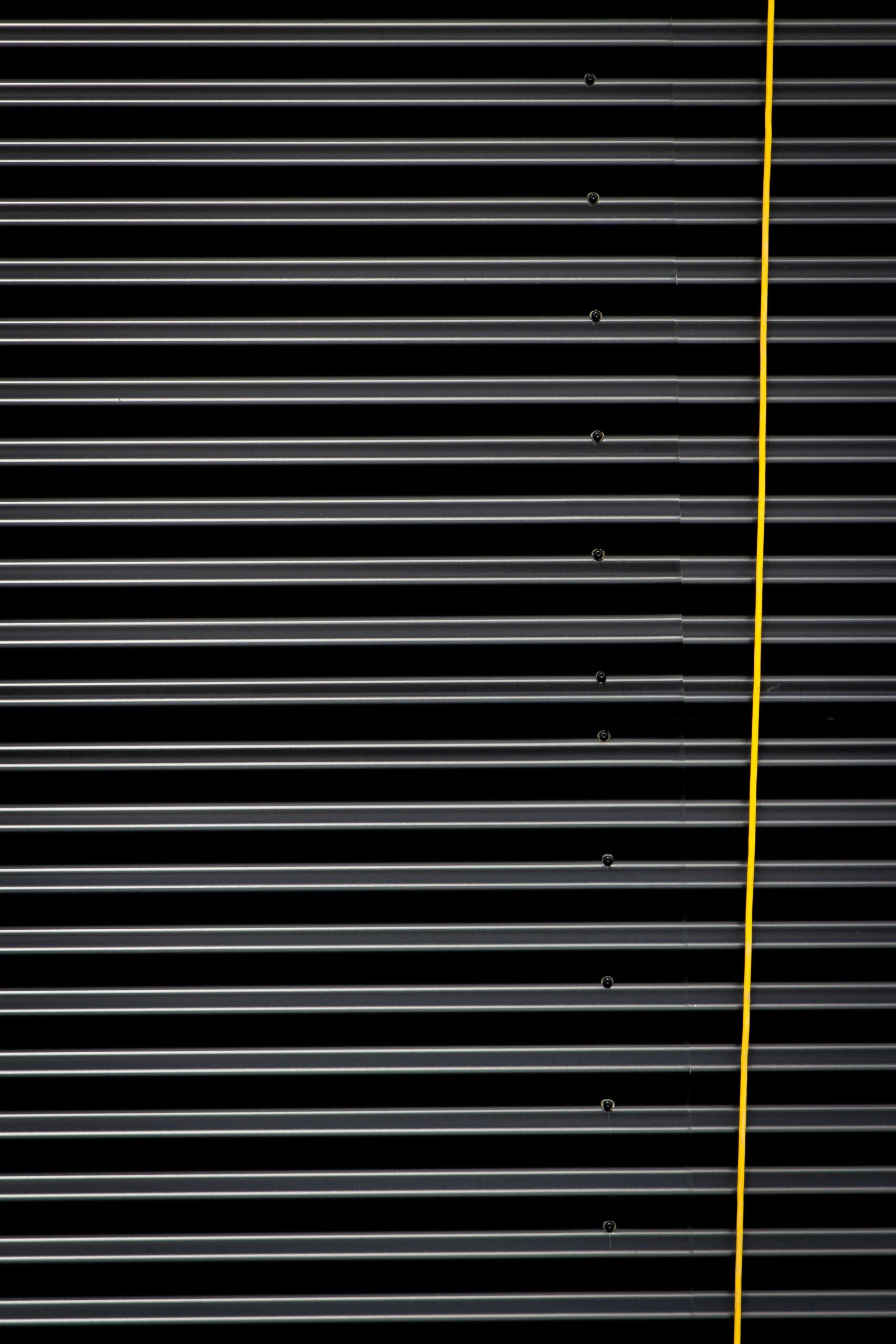 Close-up of a corrugated metal panel with a bold yellow cable, showcasing striped textures and industrial design.