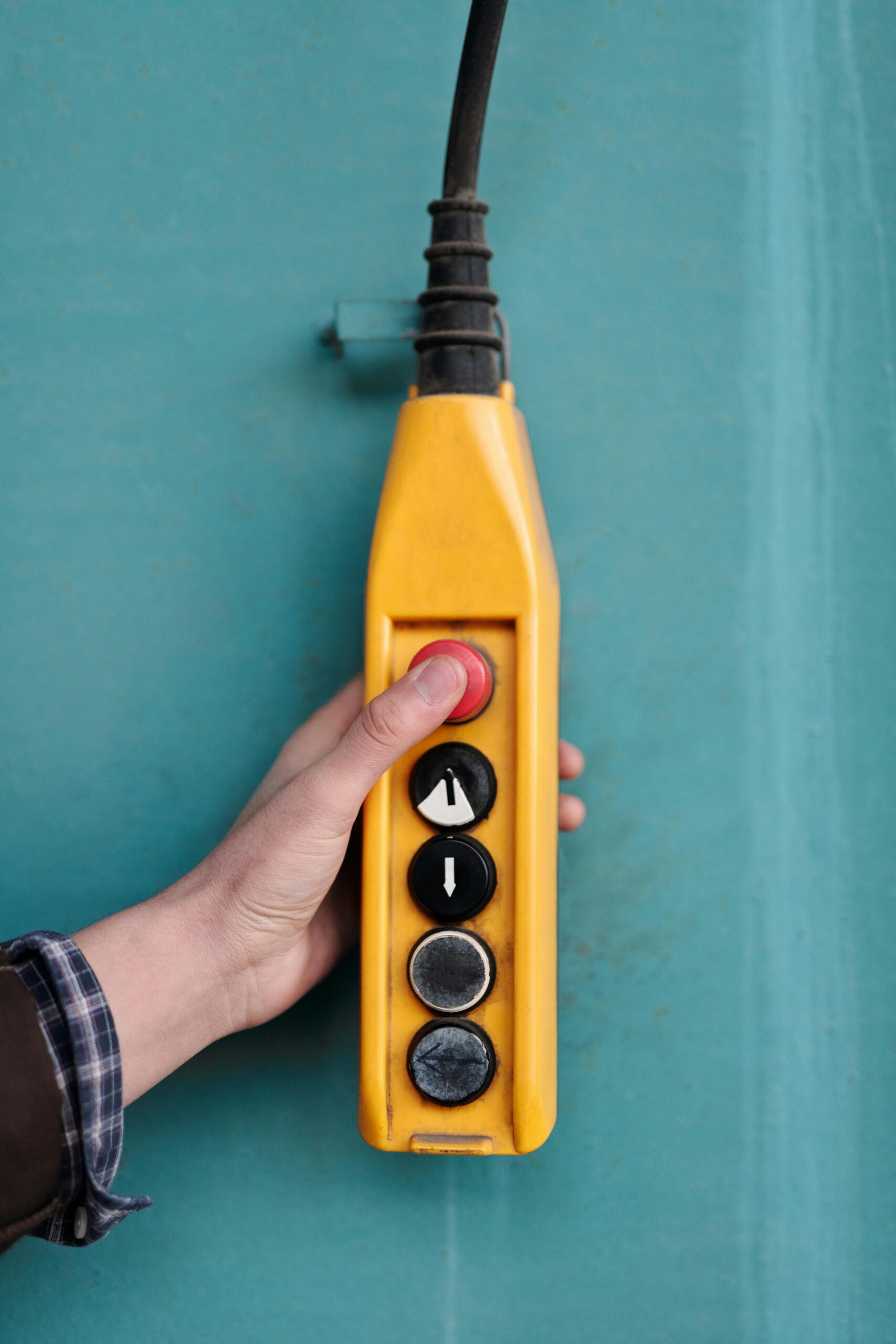A hand pressing a button on a yellow industrial control panel with directional arrows.